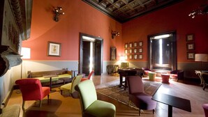 Un salon spacieux doté d’un plafond haut, de grandes fenêtres et de différents types de sièges, notamment des fauteuils et un canapé.