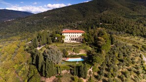 Un grand bâtiment historique, entouré d’une végétation luxuriante et de collines.