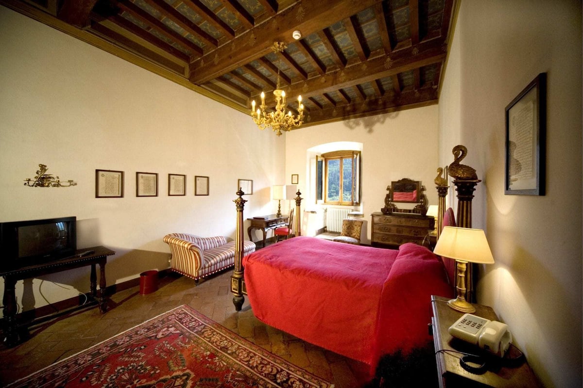 Un dormitorio con una cama grande, techo de madera, candelabro, televisor, escritorio y ventana.