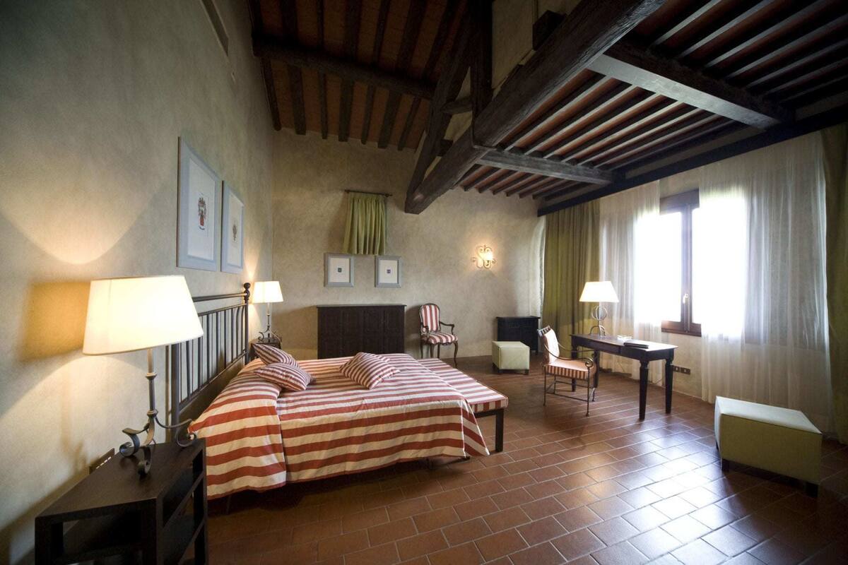 Una habitación con una cama, dos sillones, una mesa y una chimenea.