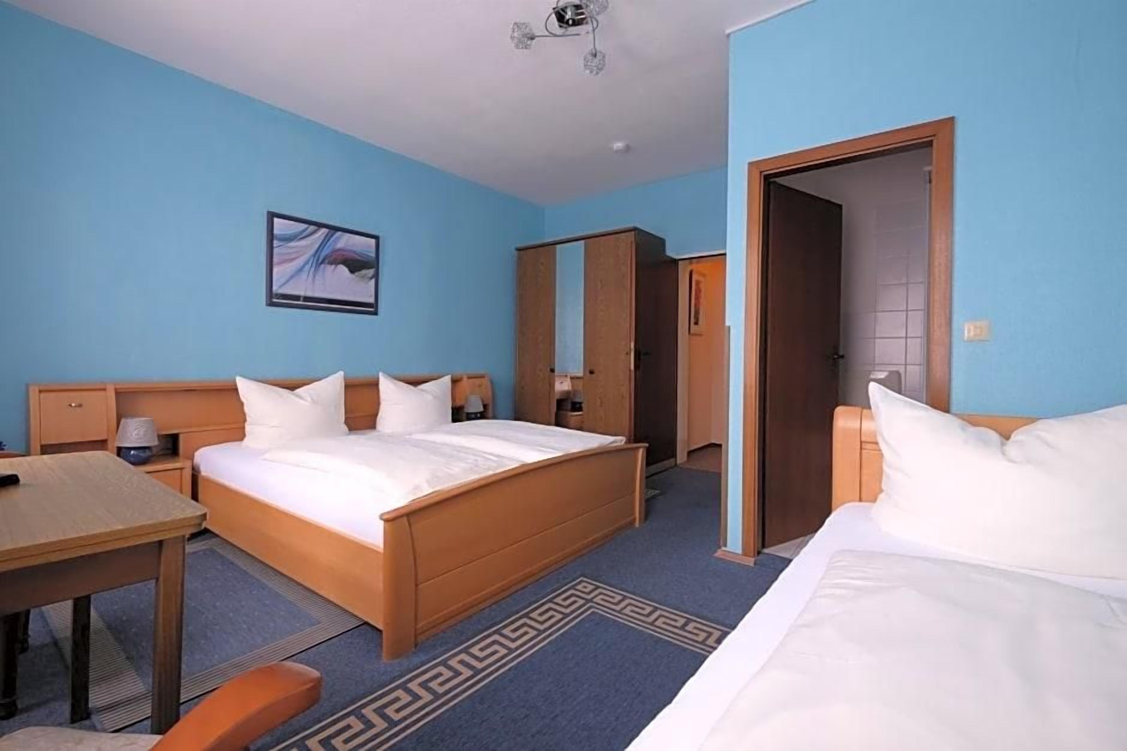 Ein Hotelzimmer mit einem Bett, einem Schreibtisch, einem Stuhl, einem Kleiderschrank und einer Tür zu einem anderen Raum.