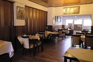 A restaurant with wooden paneling, multiple tables, chairs, and a chandelier.