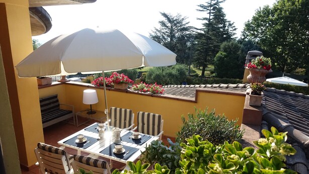 An outdoor patio with a table set for dining, striped chairs, a white umbrella, and potted plants. - Villa Pali (Marsciano)