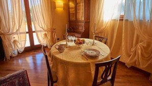 A dining area with a round table set for four, a wooden cabinet, and sheer curtains. - Villa Pali (Marsciano)