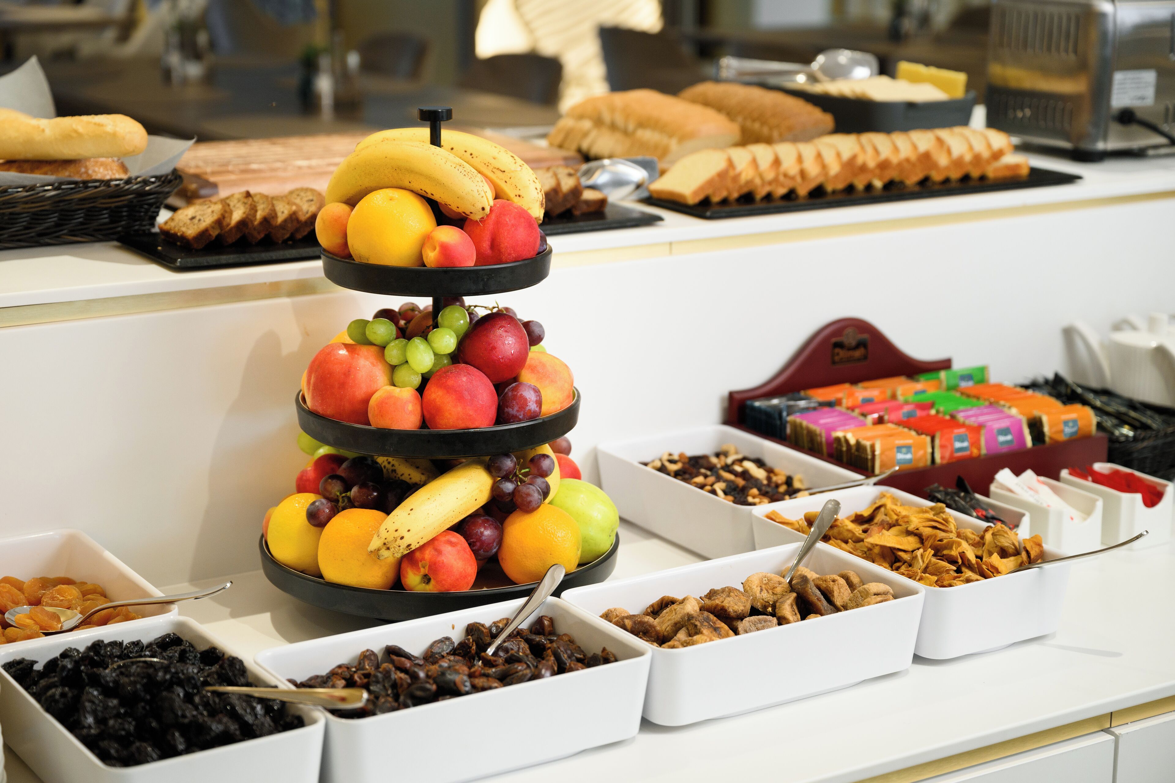 A buffet with various food items including fruits, bread, and pastries.