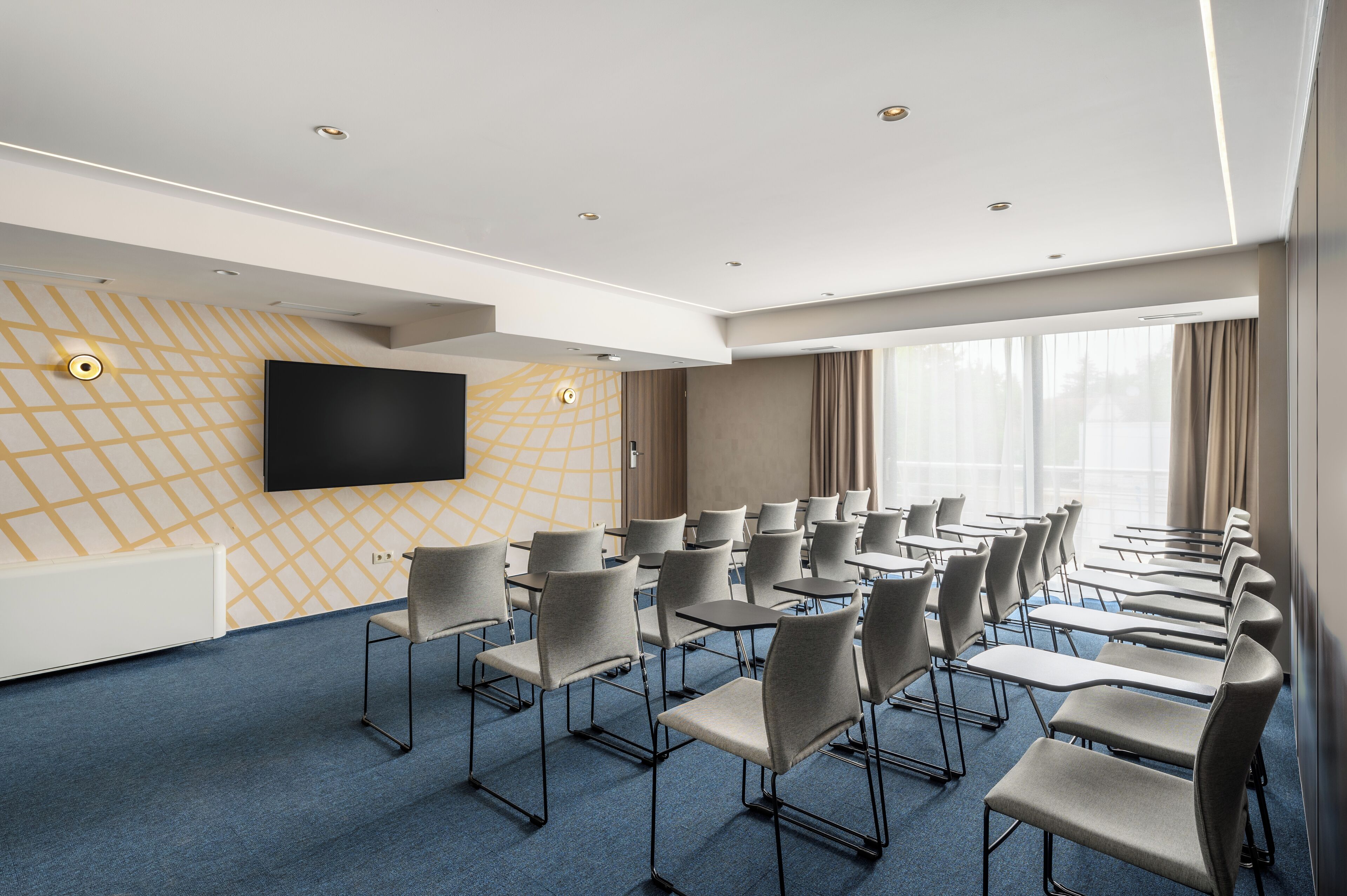 Un salón de conferencias con filas de sillas, un televisor de pantalla plana grande y un papel tapiz con diseño.