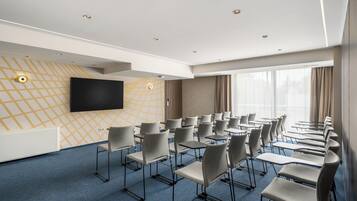 A conference room with rows of chairs, a large flat-screen TV, and a patterned wall.