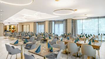 A modern dining area with multiple tables and chairs, large windows, and contemporary lighting fixtures.