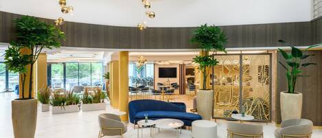 A modern lobby with a blue sofa, round tables, and potted plants.