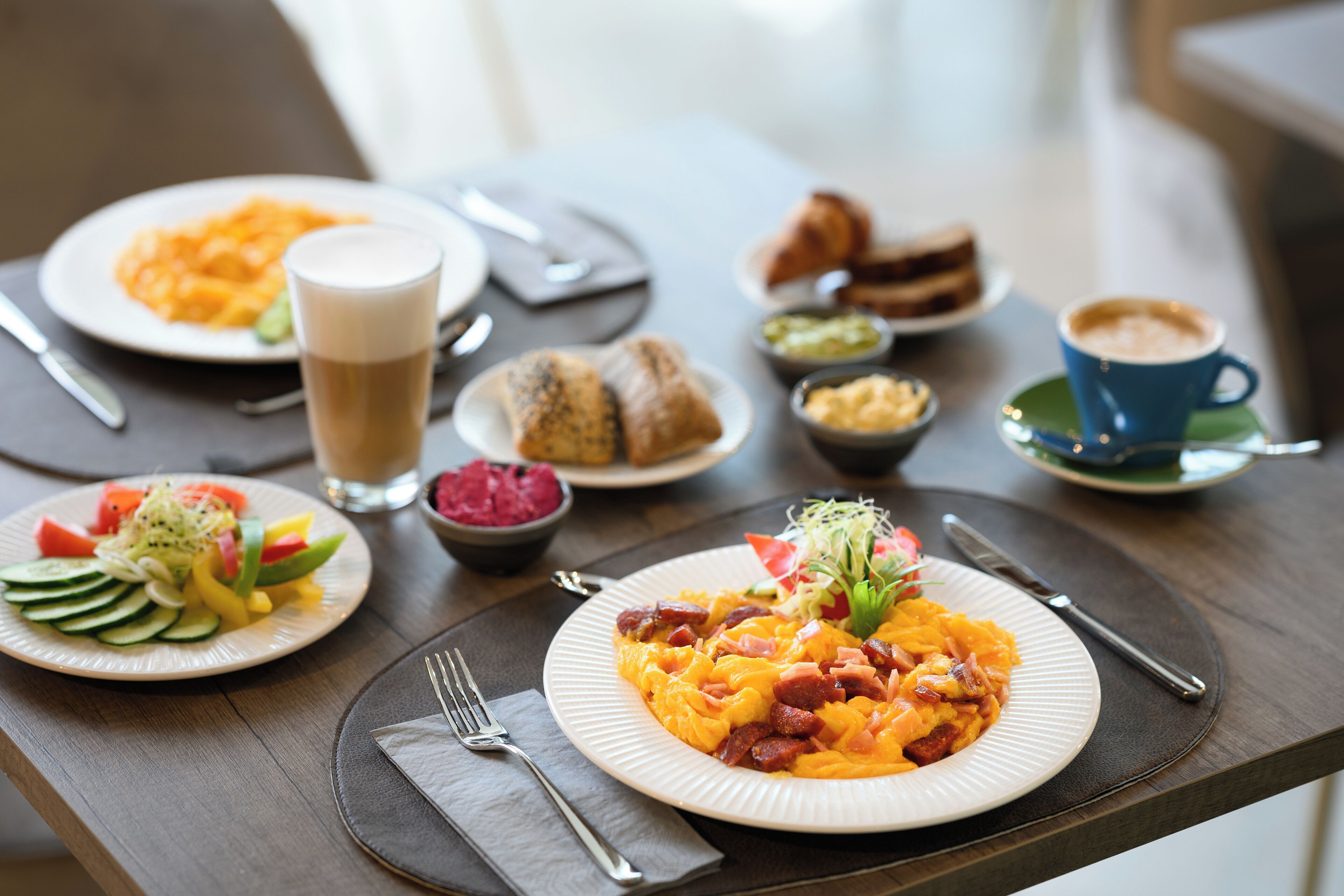 Un desayuno servido en una mesa de madera, con platos de comida, una taza de café y un vaso de leche.