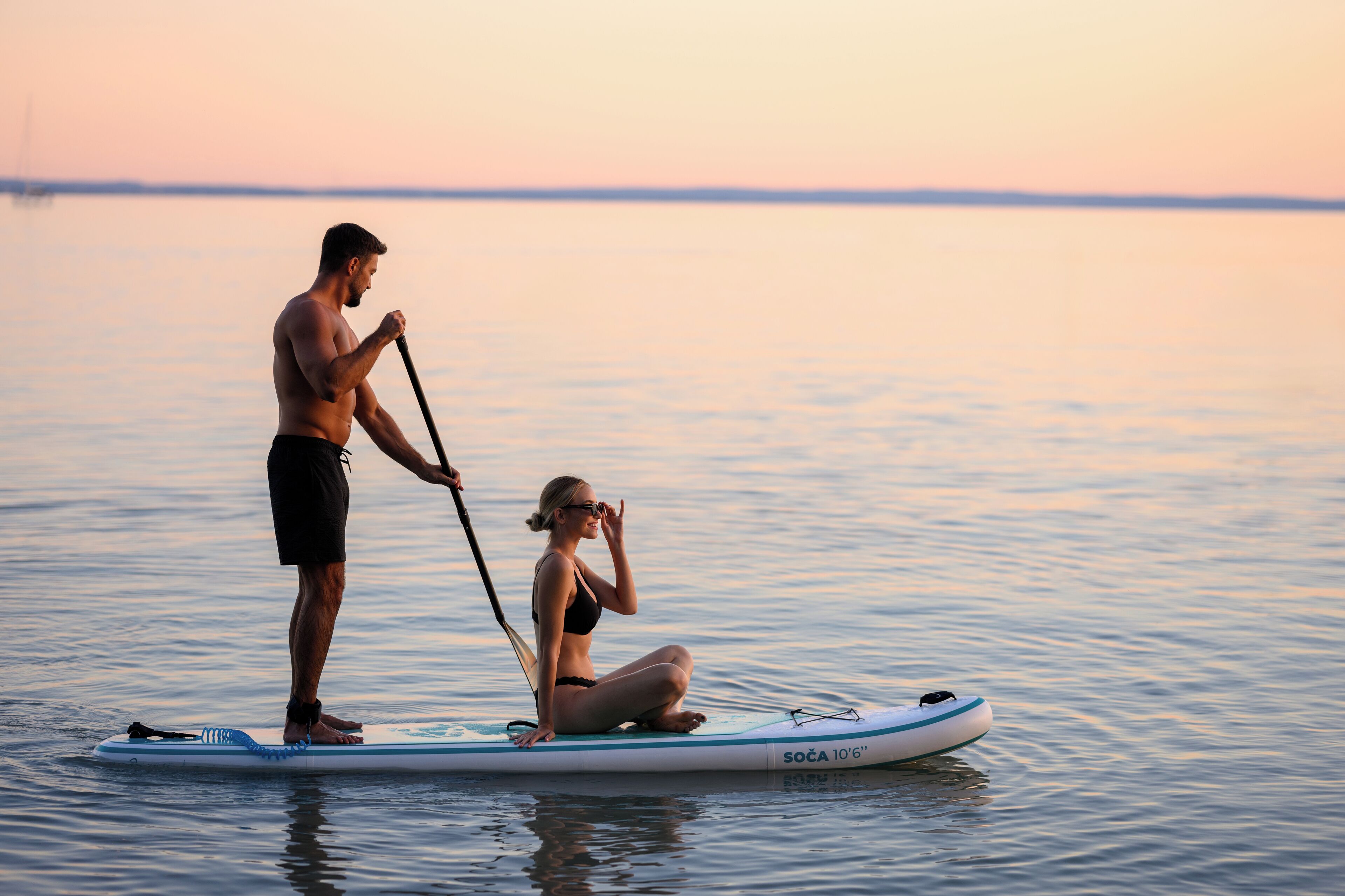 A man and a woman on a paddleboard in calm waters.