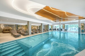 Una piscina interior moderna con sillones de descanso y un diseño de techo de madera.