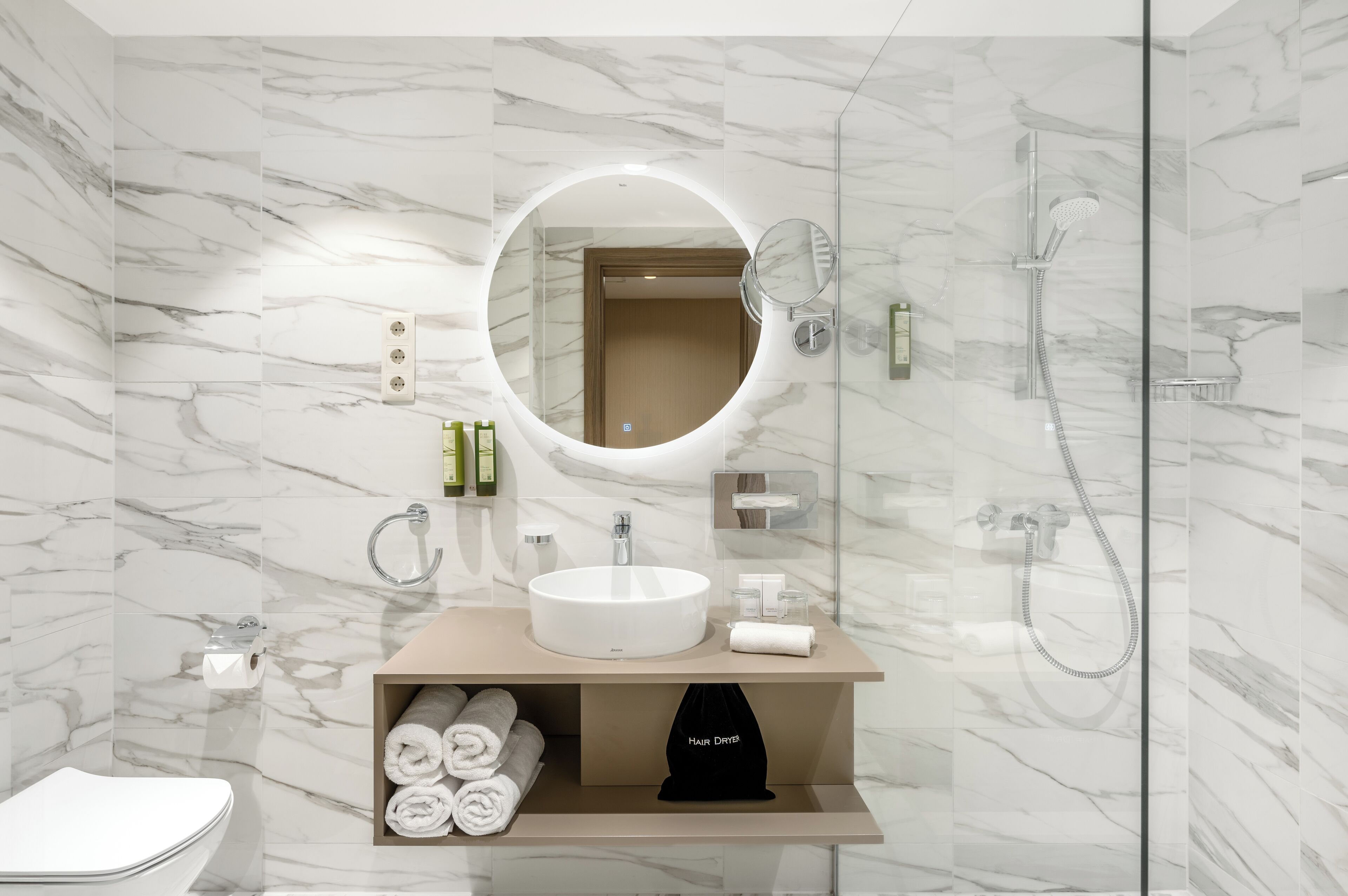 A modern bathroom with a marble wall, a round mirror, a sink, and a shower.