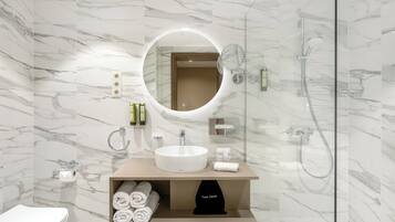 A modern bathroom with a marble wall, a round mirror, a sink, and a shower.