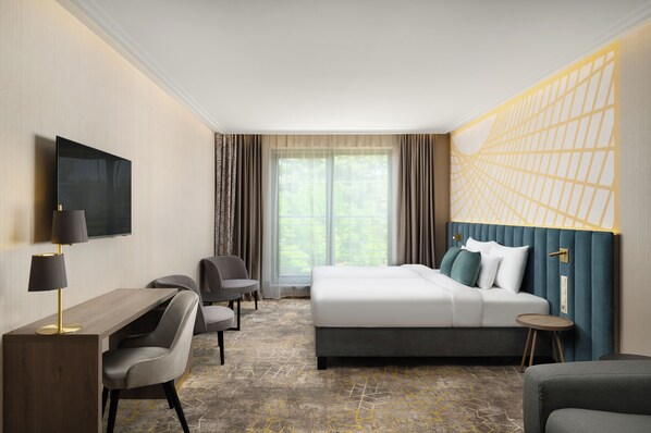 A hotel room with a bed, desk, chairs, and a TV.