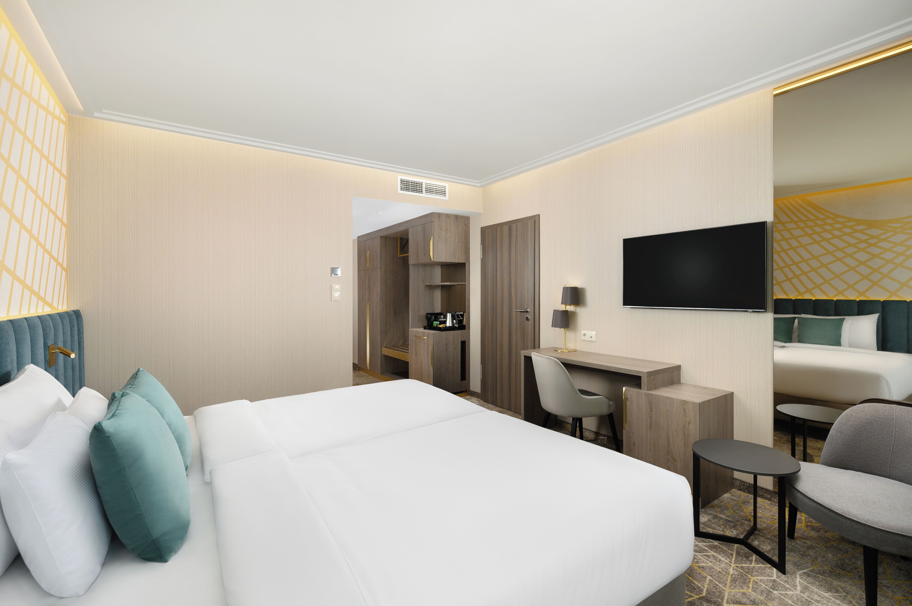 A hotel room with a large bed, a desk, a chair, a TV, and a small table.