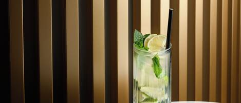 A clear glass with a straw, lime slice, and mint leaves on a marble surface against a striped background.