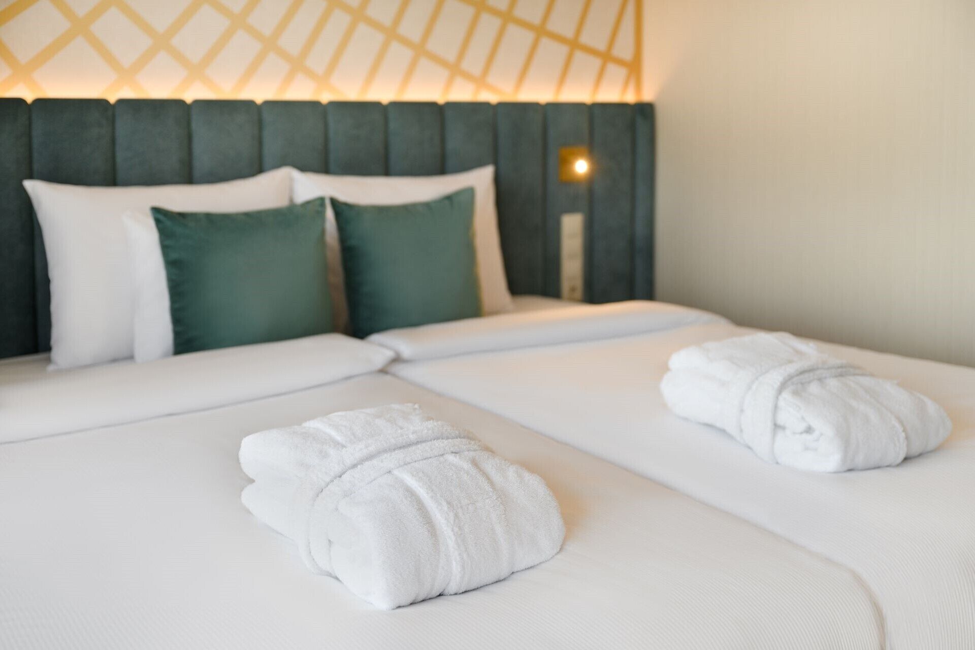 A neatly made bed with white linens and two rolled towels.