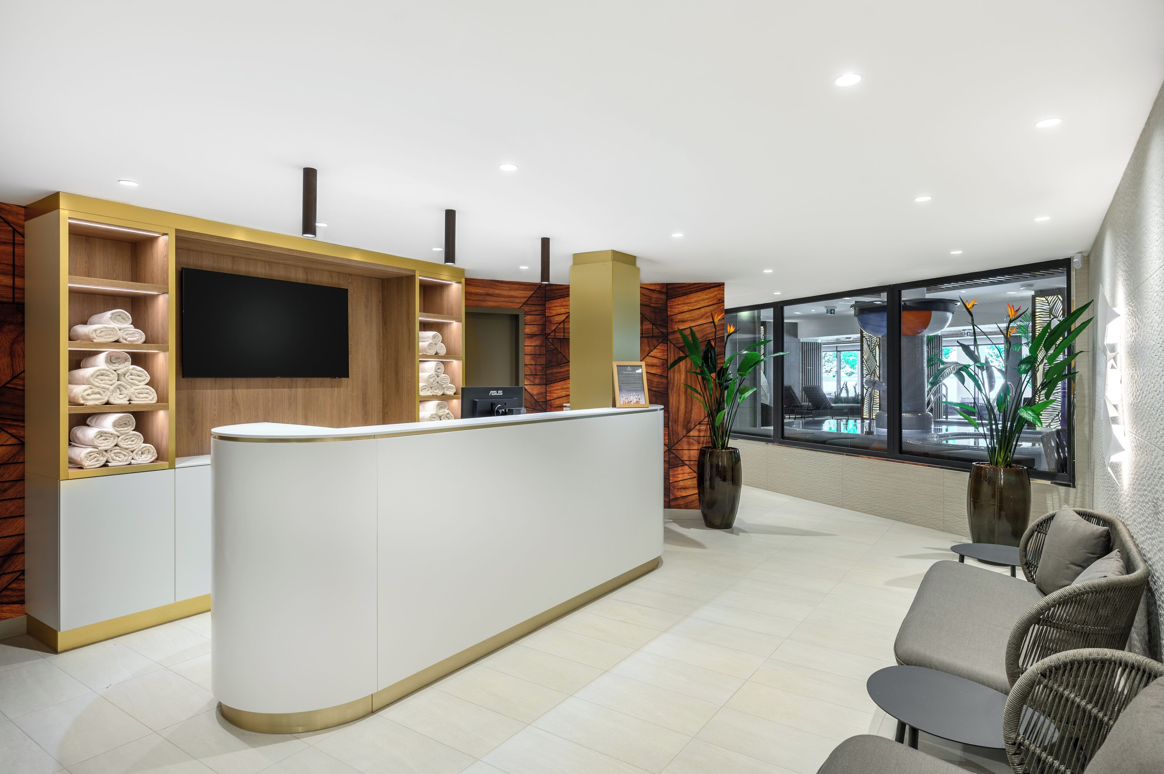 Un área de recepción con un mostrador blanco, estanterías de madera con toallas, un televisor de pantalla plana y un ventanal con vistas al exterior.