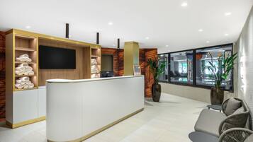 Un área de recepción con un mostrador blanco, estanterías de madera con toallas, un televisor de pantalla plana y un ventanal con vistas al exterior.
