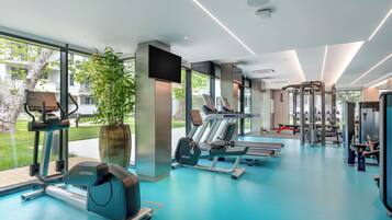 A modern gym with cardio machines, weightlifting equipment, and large windows offering views of the outdoors.