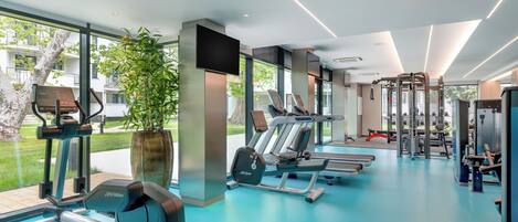 A modern gym with cardio machines, weightlifting equipment, and large windows offering views of the outdoors.