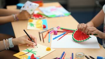 A table with various art supplies and a person drawing on a piece of paper.