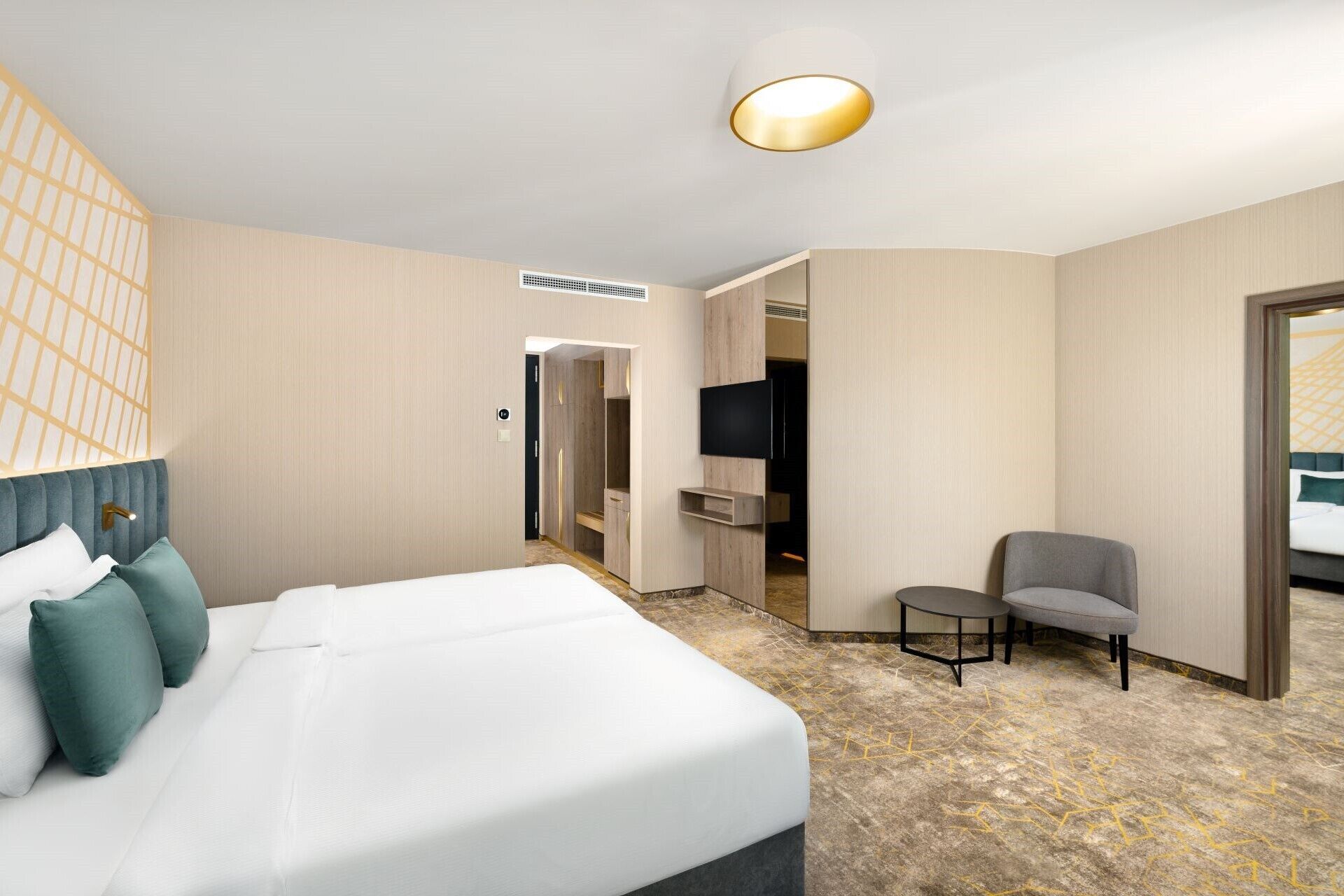 Ein Hotelzimmer mit einem Bett, einer Sitzecke, einem Fernseher und einer Tür zu einem weiteren Raum.