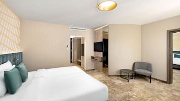 Ein Hotelzimmer mit einem Bett, einer Sitzecke, einem Fernseher und einer Tür zu einem weiteren Raum.