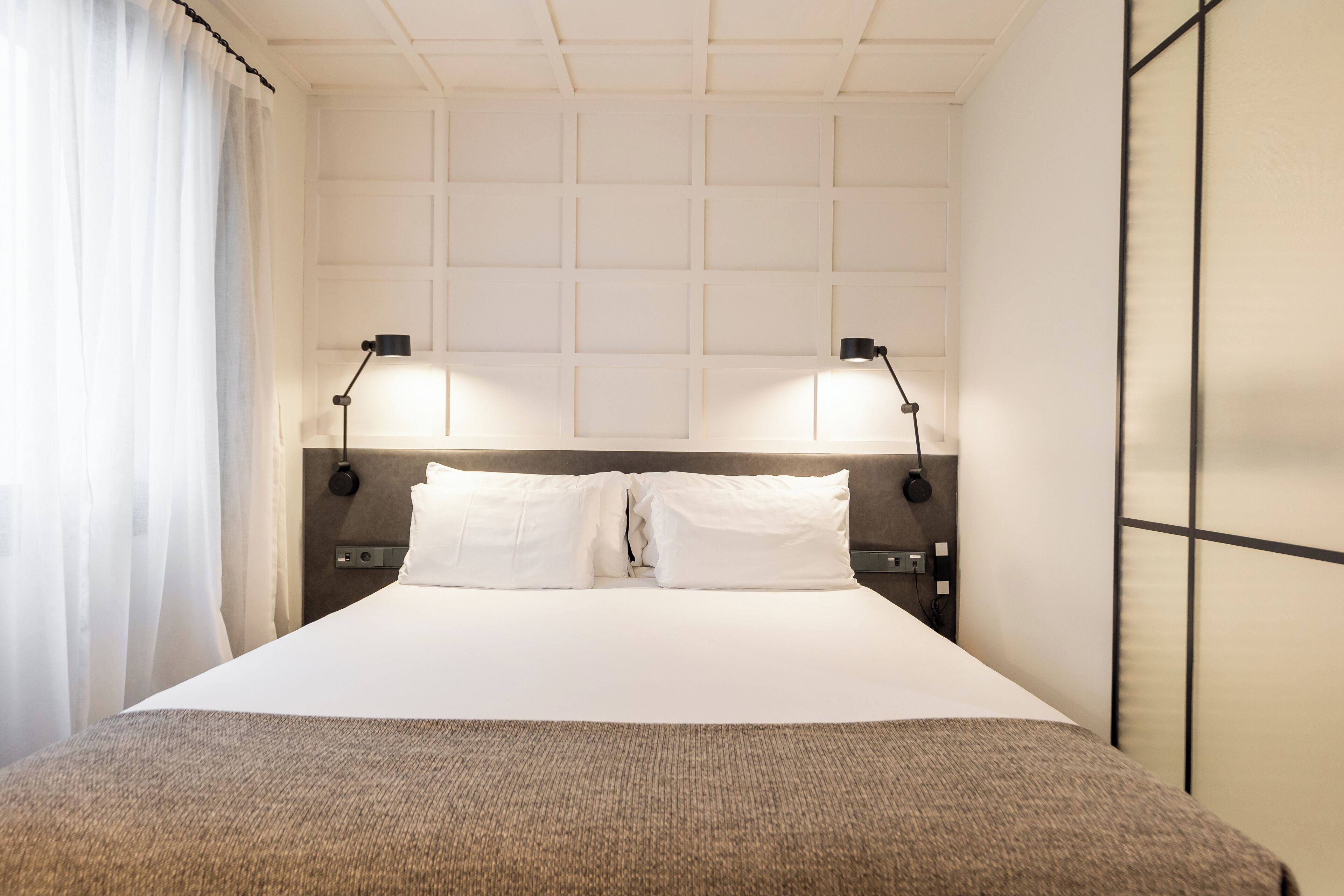 Ett hotellrum med en stor säng, två sänglampor, en sänggavel och ett fönster med gardiner.