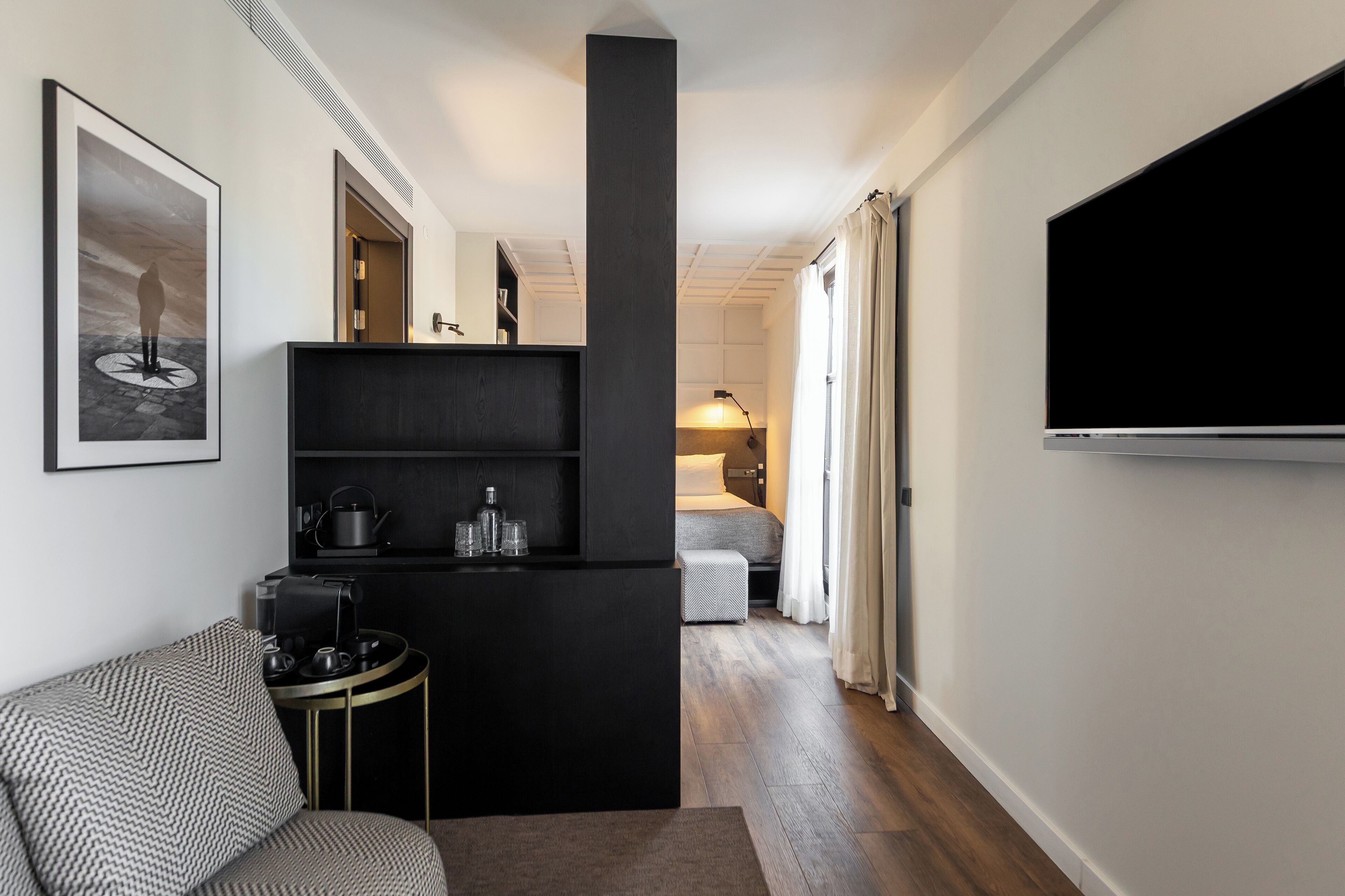 A modern hotel room with a black console table, a sofa, a TV, and a bed with a nightstand.