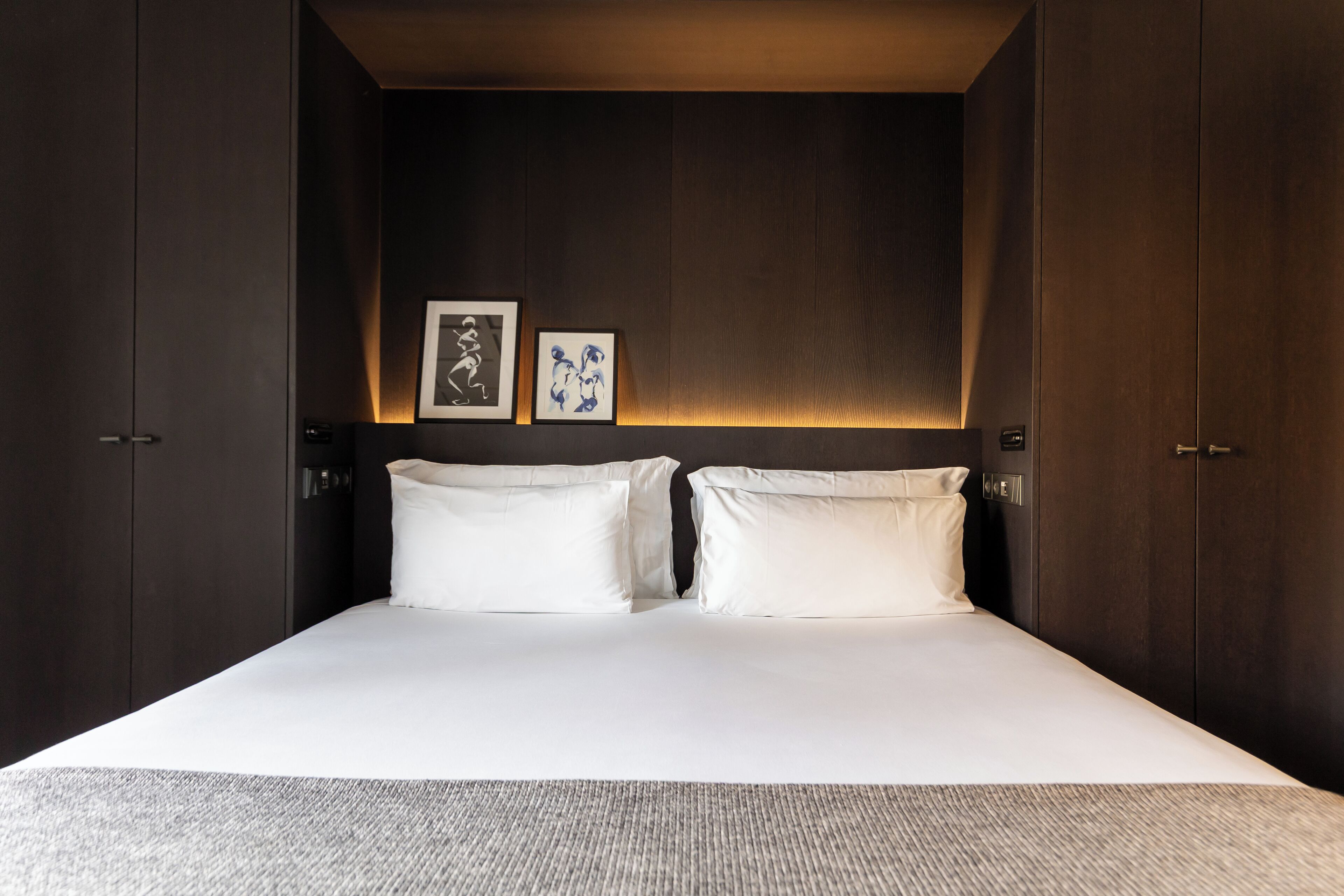 A modern hotel room with a large bed, dark wood paneling, and two framed artworks on the wall.