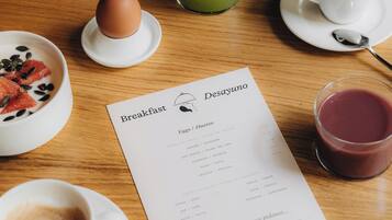 Une table en bois dressée pour le petit-déjeuner, avec un menu, une assiette de raisins, un verre de jus vert, une tasse de café et un sandwich.