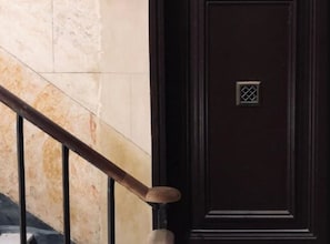 A dark wooden door with a small window, a marble staircase with a metal handrail, and a textured wall.