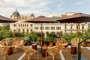 A rooftop terrace with wicker furniture, potted plants, and umbrellas. - Yurbban Ramblas Boutique Hotel (Barcelona)
