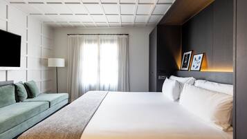 A modern hotel room with a large bed, a green sofa, a flat-screen TV, and a wall-mounted lamp.