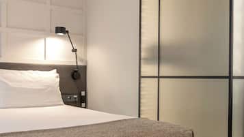 Una cama bien hecha con una almohada blanca y una manta gris, una lámpara de noche y una mesita de noche negra.