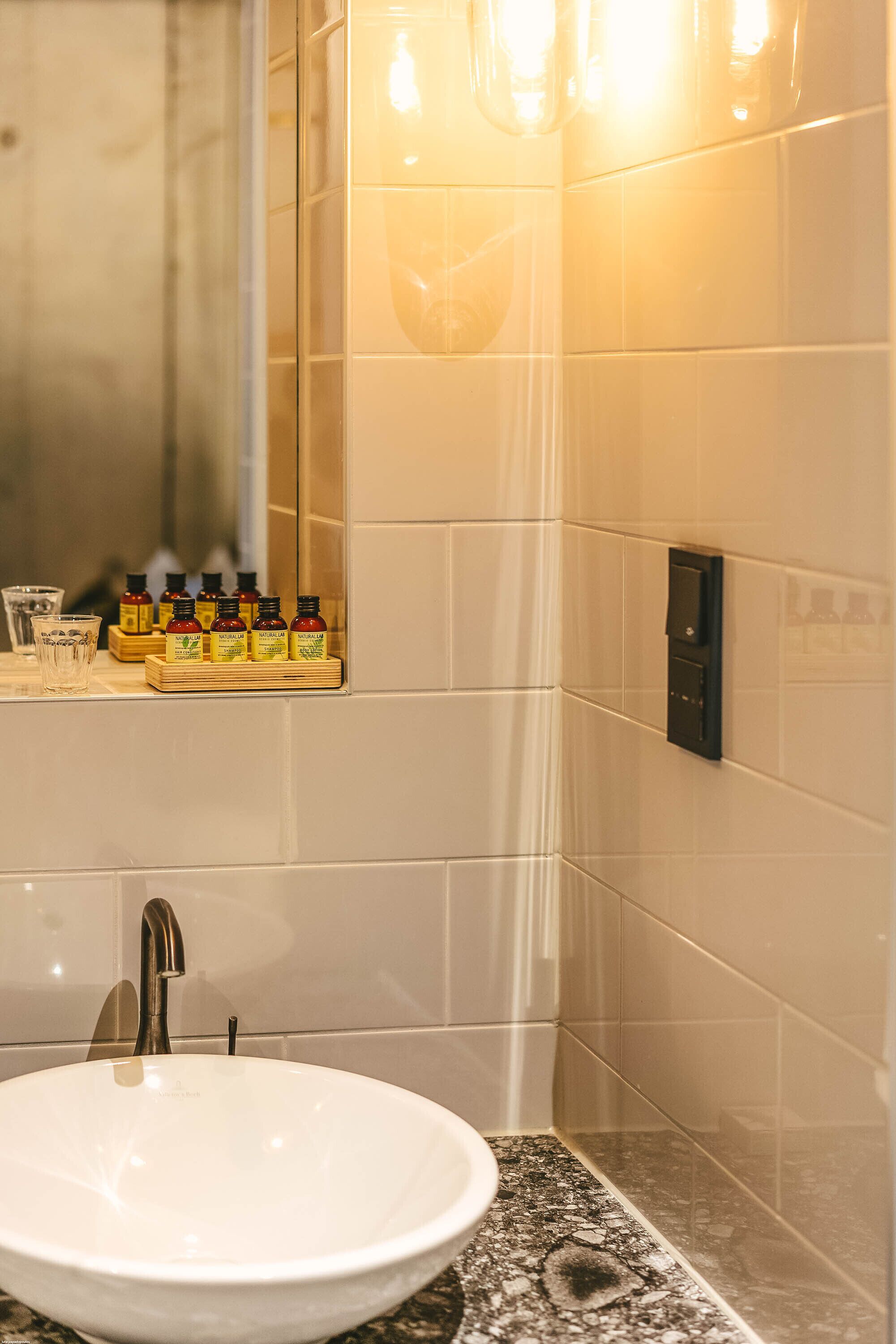 Un baño con lavamanos blanco, un espejo y una repisa con artículos de aseo.