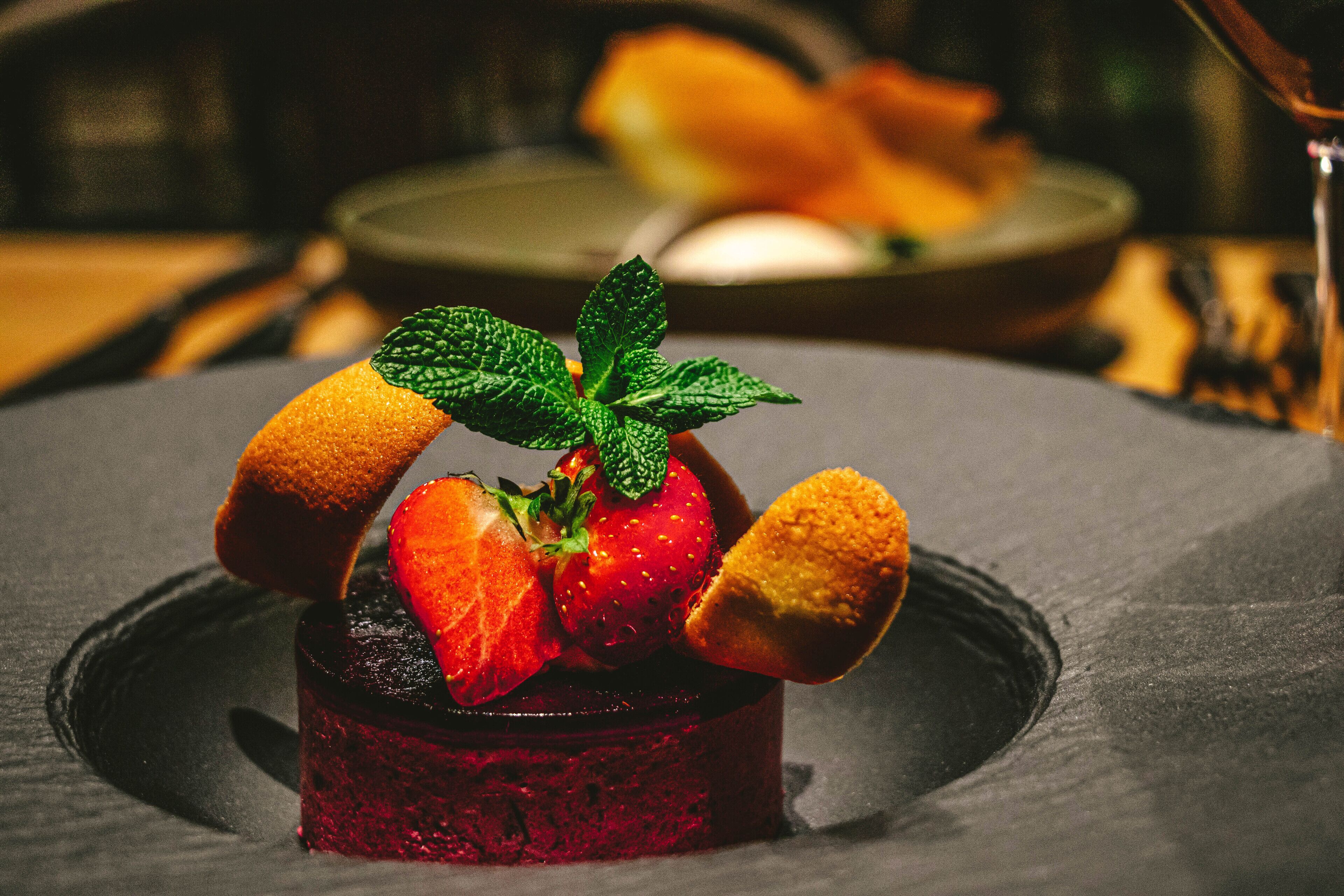 Un dessert aux fraises et aux feuilles de menthe, présenté sur une assiette foncée.