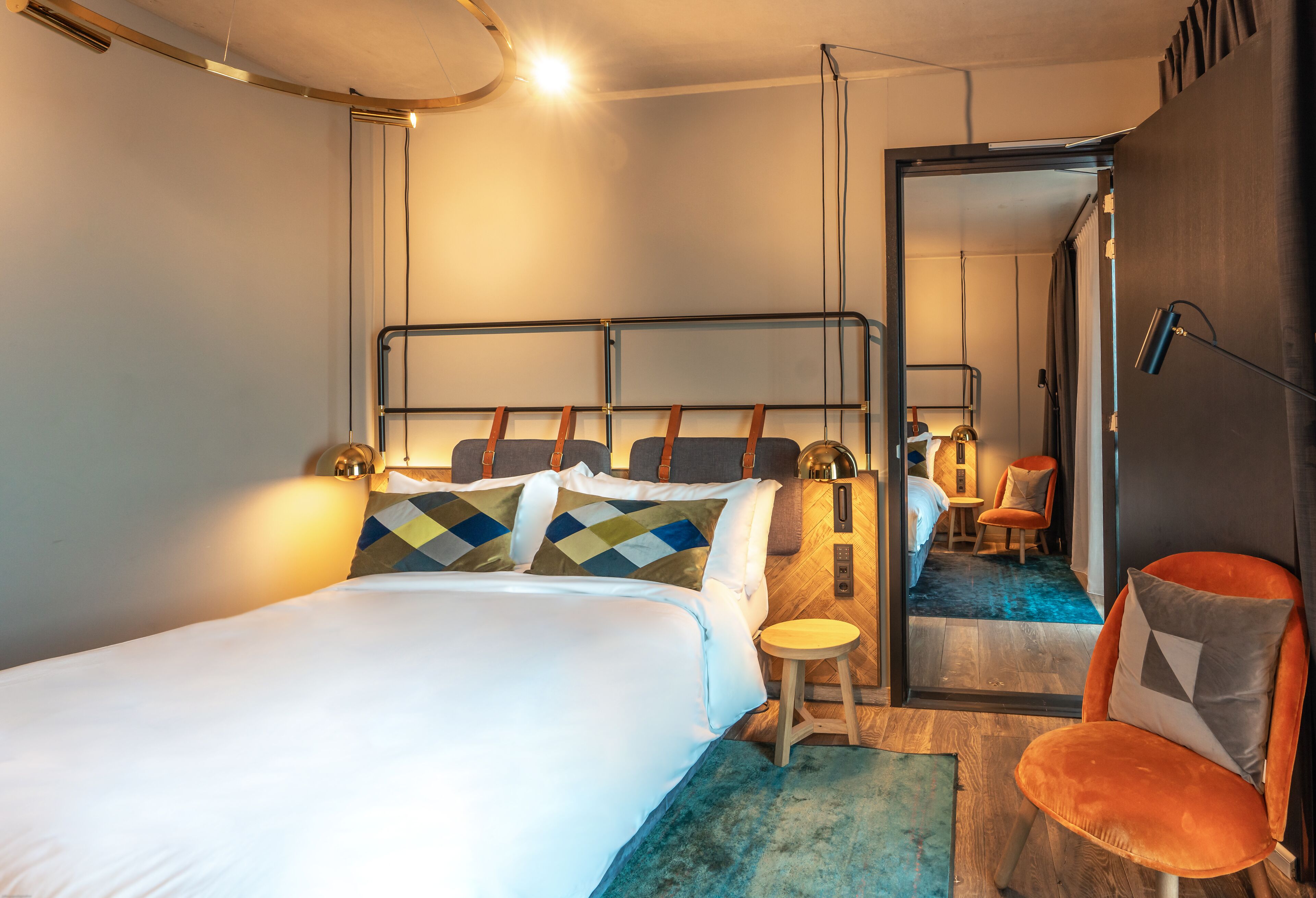Una habitación de hotel moderna con una cama grande, un taburete pequeño, una silla y un espejo.