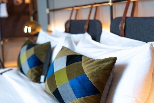Una cama con sábanas blancas y una almohada de cuadros.