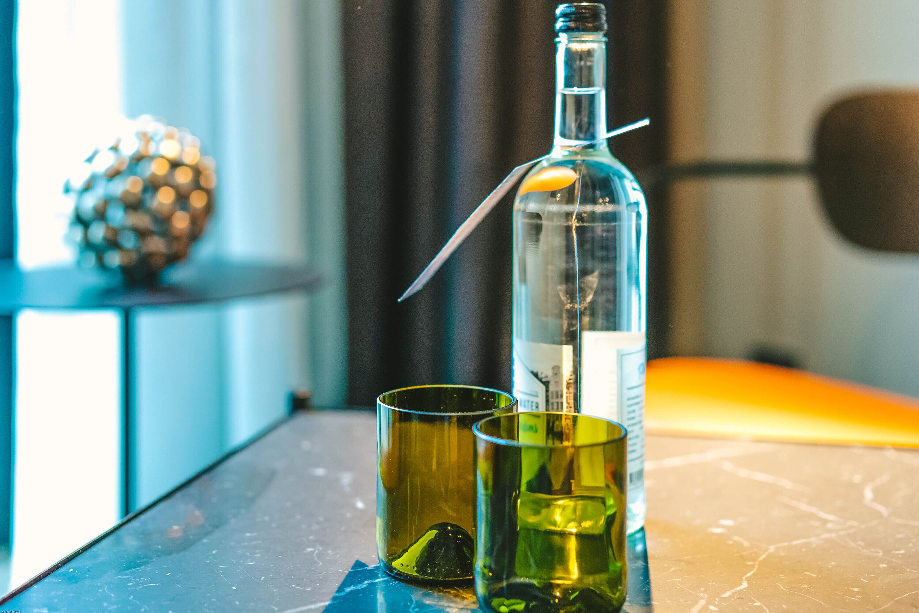 A bottle of alcohol with a straw, two glasses, and a decorative sphere on a table.