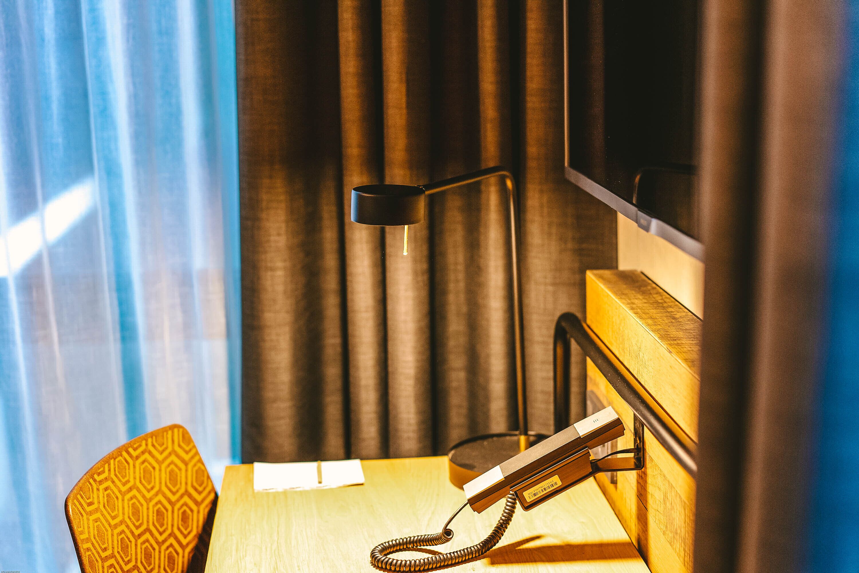 Una habitación de hotel con escritorio, teléfono, lámpara y televisión.