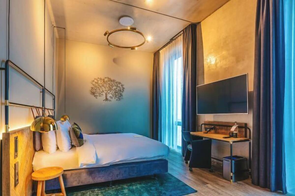 A modern hotel room with a bed, desk, TV, and large windows.