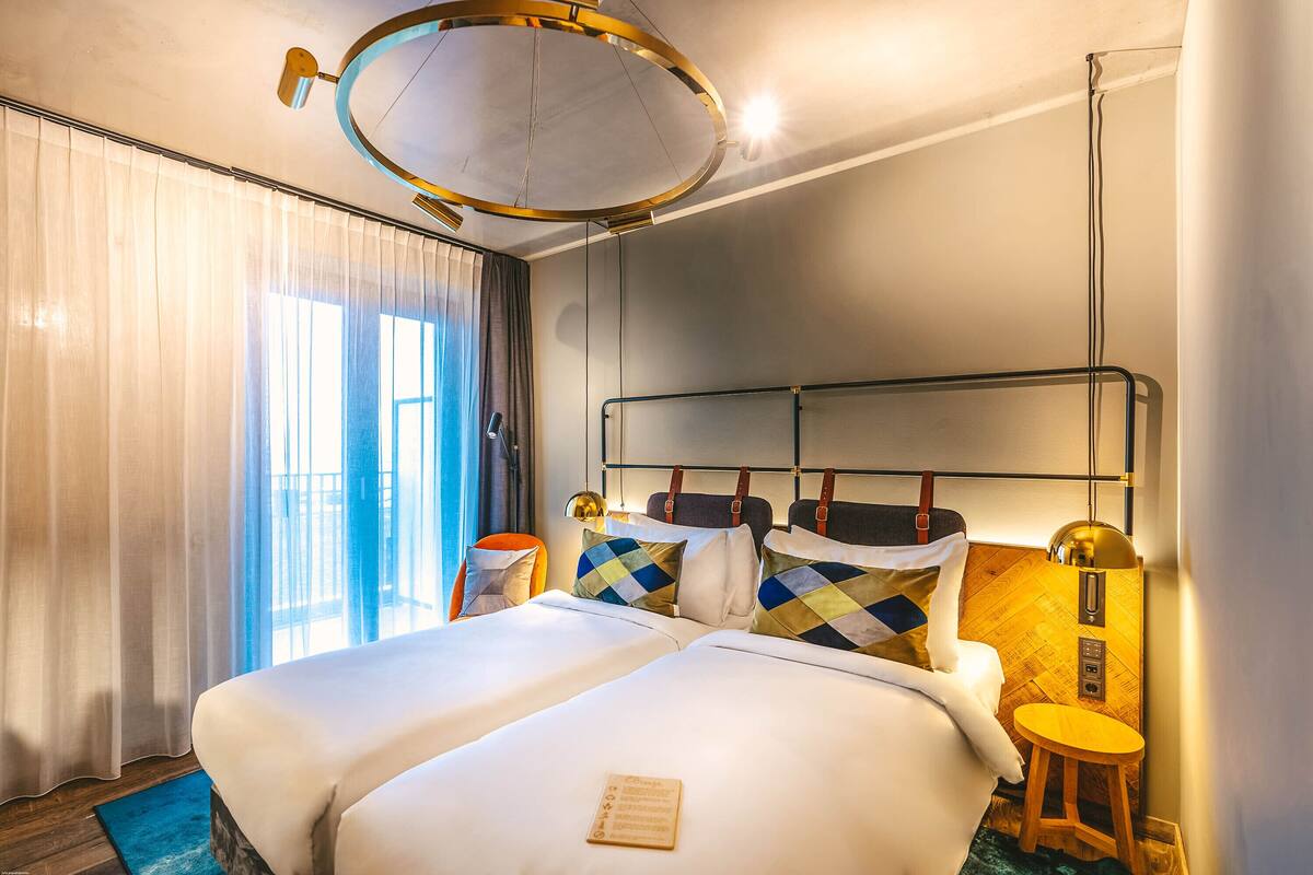A hotel room with a large bed, a small stool, a desk, and a mirror on the wall.