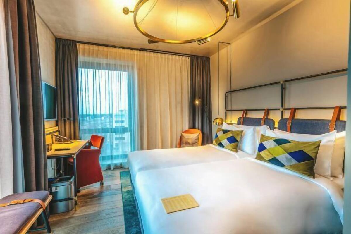 A hotel room with a large bed, a desk, a chair, and a view of the city.