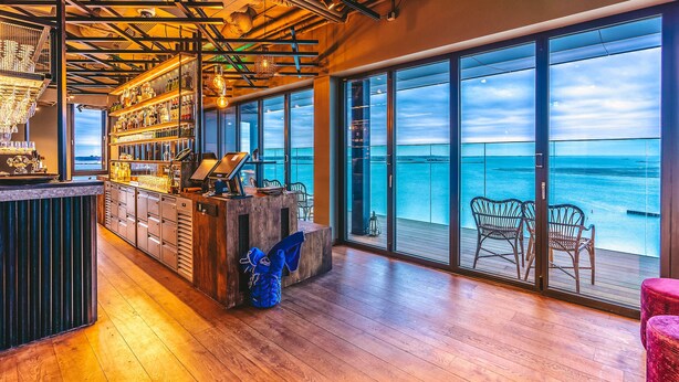 A bar area with a view of the ocean through large windows. - Four Elements Hotel Amsterdam (Amsterdam)