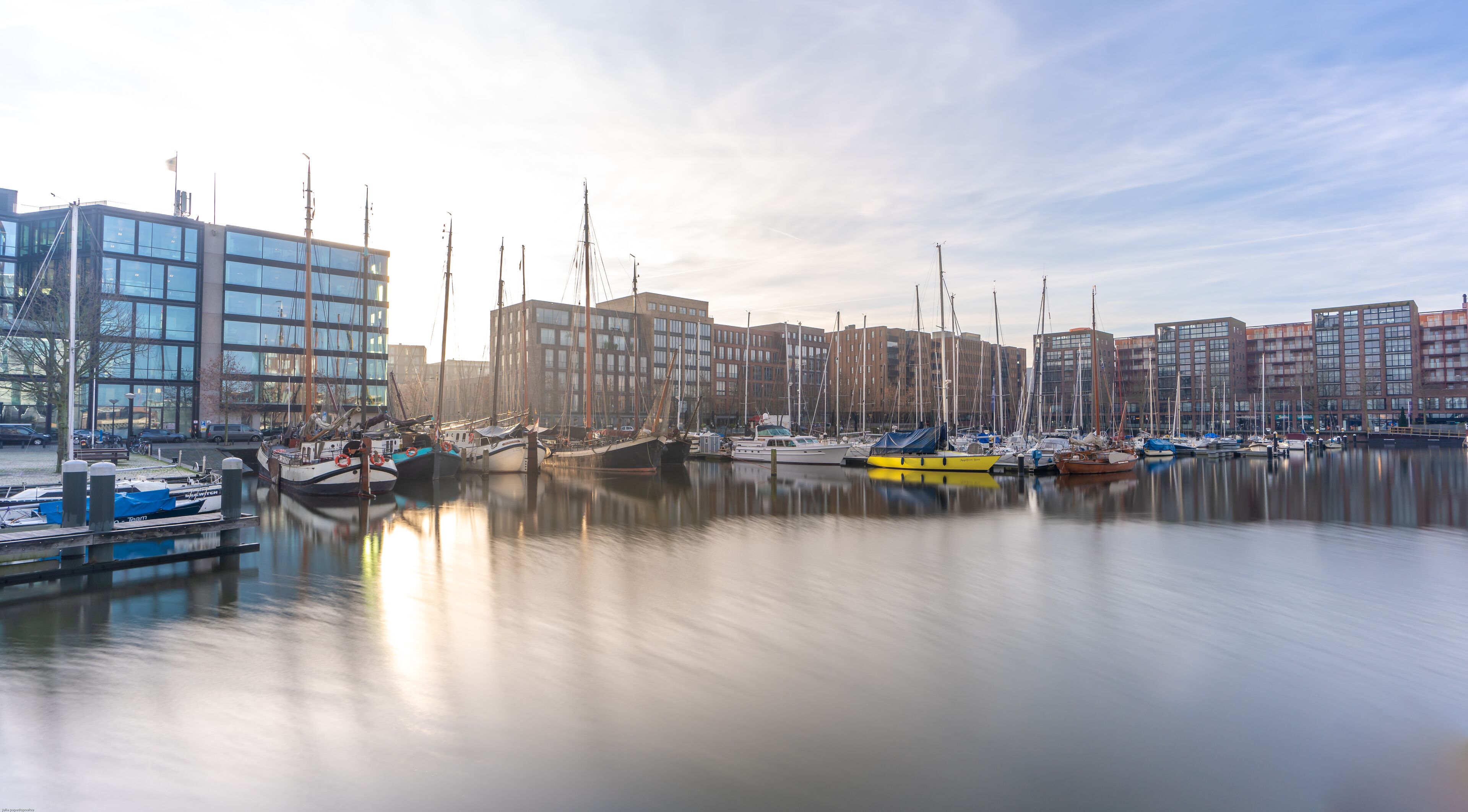Un port de plaisance où sont amarrés des bateaux, entouré de bâtiments modernes.