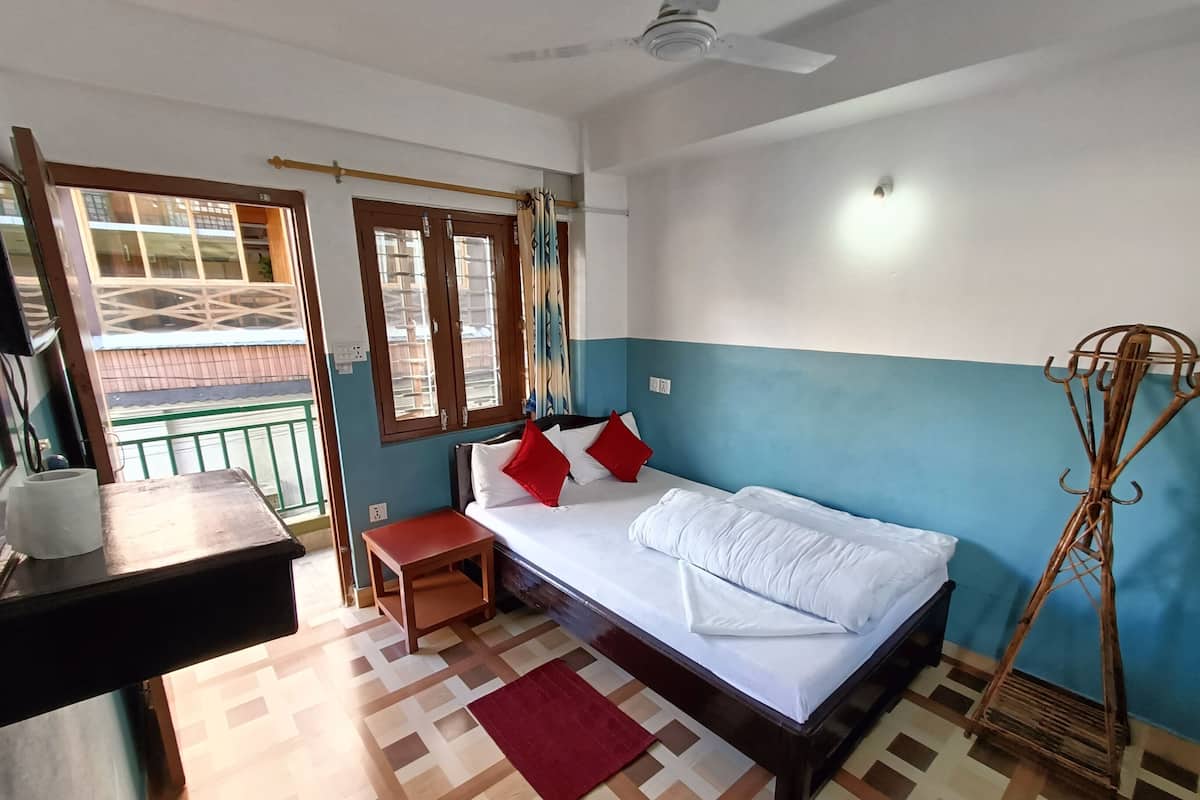 A bedroom with a bed, a small table, a bench, a ceiling fan, and a window with curtains.