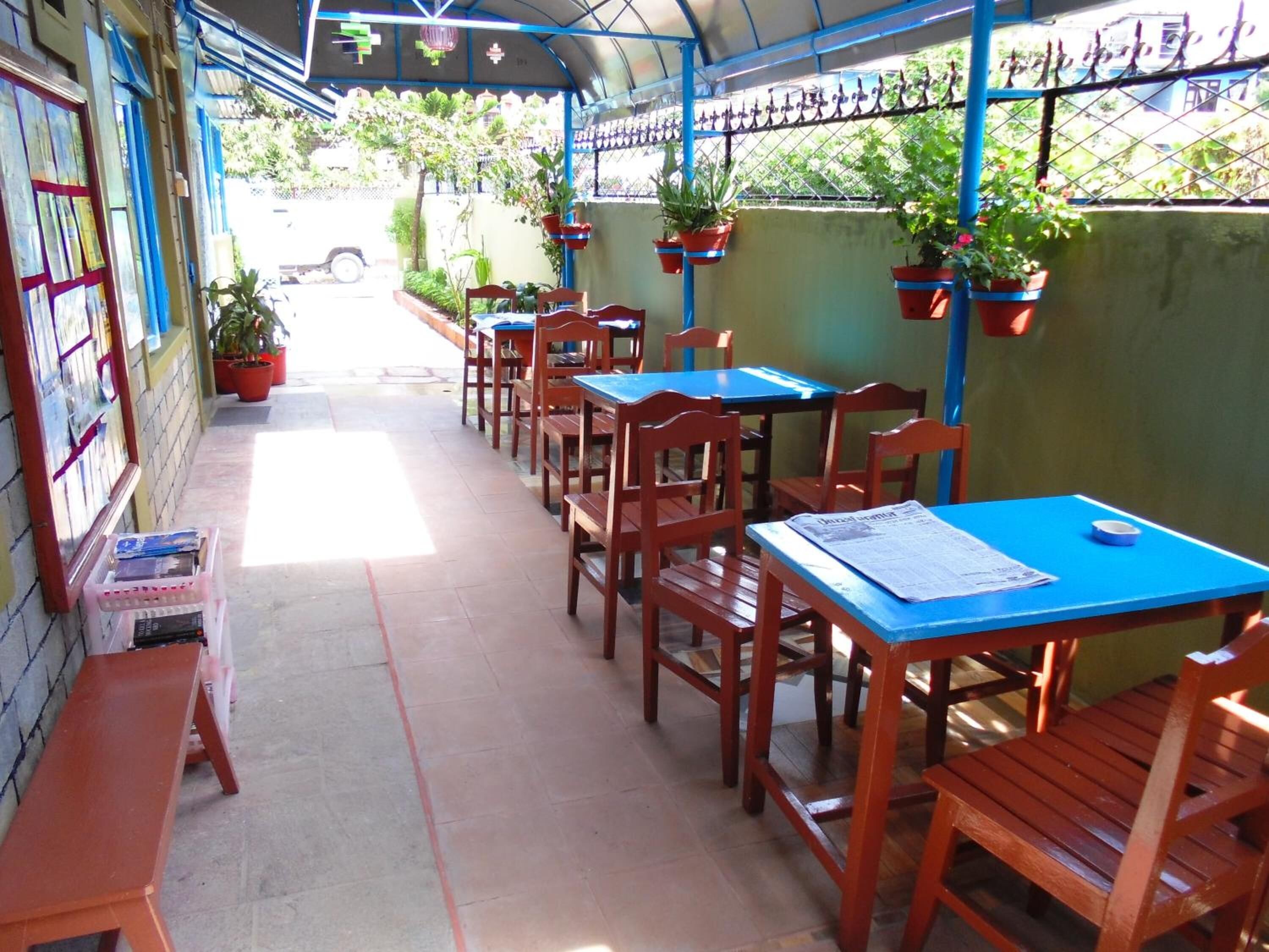 An outdoor patio with wooden tables and chairs, potted plants, and a tiled floor.